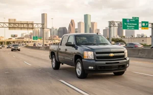 A gray 2007 Chevrolet Silverado 1500 driving on a Houston highway with the downtown city skyline and I-45 South road signs in the background, showcasing the classic truck on Texas roads.