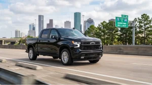 A black Chevrolet Silverado 1500 driving on a highway with the Houston skyline and I-10 road signs in the background, showcasing Chevy truck motor performance in Texas.