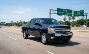A dark blue 2013 Chevrolet Silverado 1500 Crew Cab pickup driving on Highway 6 near Sugar Land, Texas, with highway overhead signs and suburban scenery in the background.
